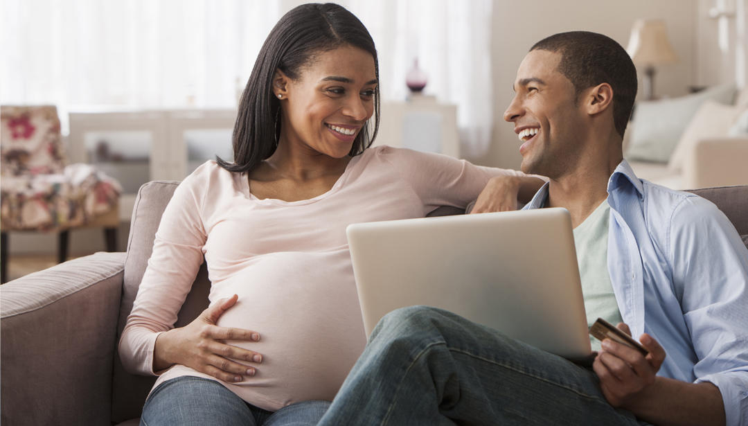 pregnant woman sitting on couch with partner looking at computer