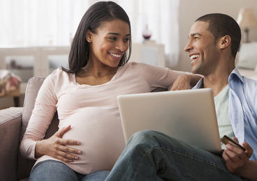 Pregnant woman sitting on couch with partner looking at computer.