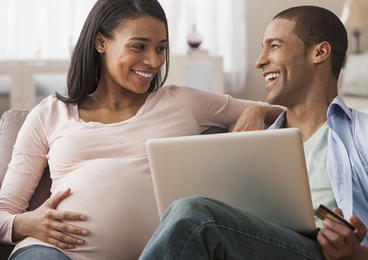 Pregnant woman sitting on couch with partner looking at computer.