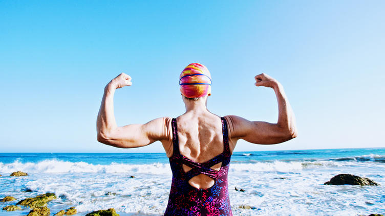 older woman from behind in bathing suit flexing muscles